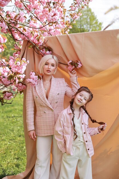 Hermosa madre con el pelo corto y blanco y su feliz hija sobre un fondo beige cerca de sakura