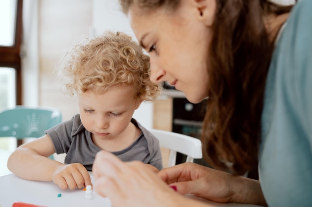 Una hermosa madre se sienta en la mesa de la cocina con su hija en edad preescolar y hace algo