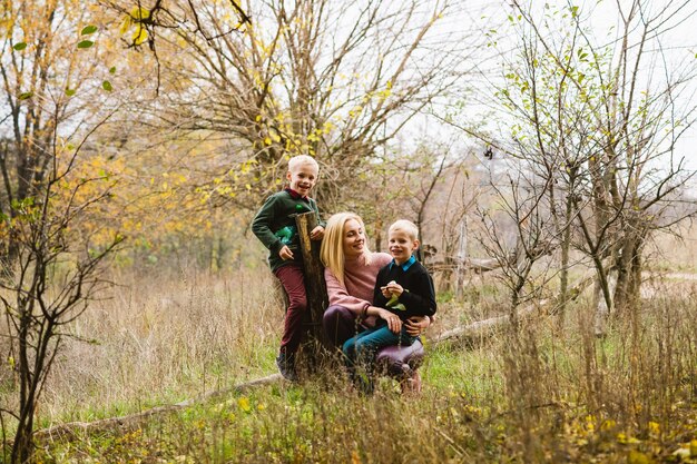 Hermosa madre soltera abraza a dos niños preadolescentes y posando en el fondo de la naturaleza de otoño, fin de semana familiar activo