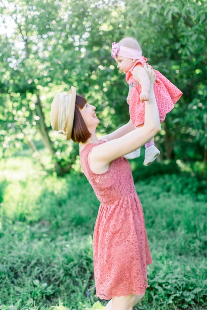 Hermosa madre con el sombrero de paja y su pequeña hija al aire libre familia mirar en un vestido rosa. aspecto familiar Joven madre vomita bebé en el cielo, en un día soleado.