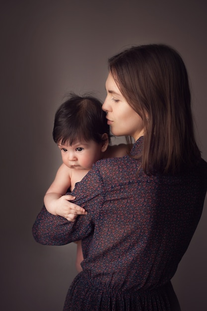 Foto una hermosa madre sostiene a su pequeño hijo desnudo en sus brazos y lo besa en la cabeza.