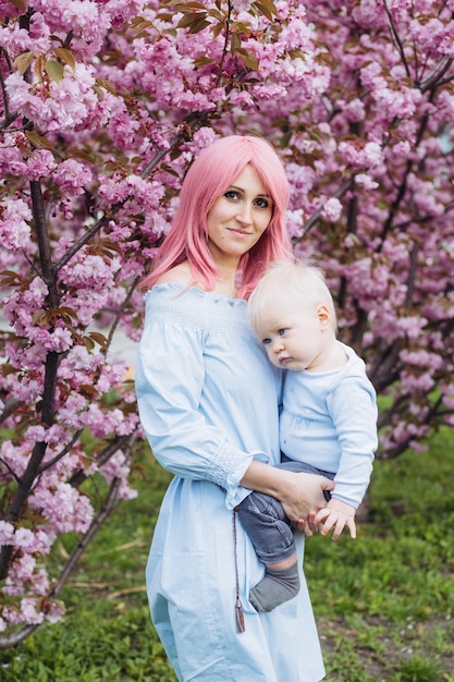 Hermosa madre sostiene en sus brazos a un pequeño hijo lindo Mamá y pequeño bebé en un jardín floreciente Sakura