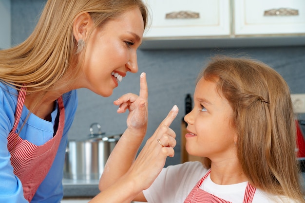 Hermosa madre y su adorable hija se divierten en la cocina mientras cocinan comida en casa