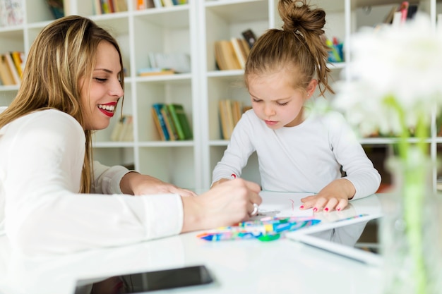 Hermosa madre con su dibujo hija con crayones en casa.