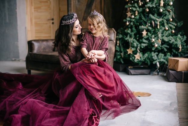 Hermosa madre y su hija en la imagen de la reina y la princesa con el vestido color Marsala con una larga cola en el desván