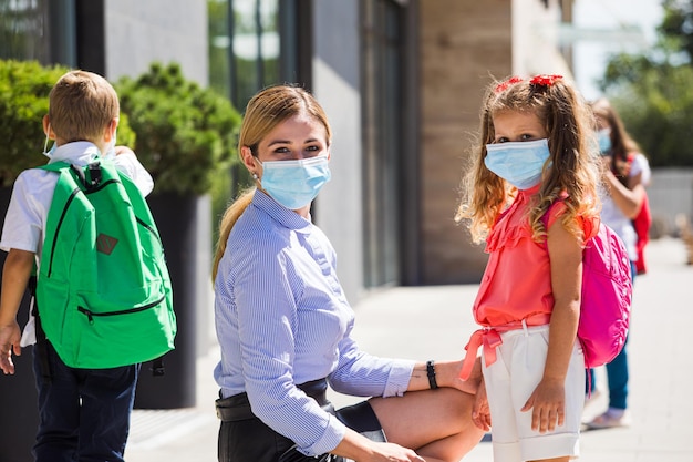 La hermosa madre con su hija con una máscara protectora mira la cámara La madre acompaña a su hija a la escuela durante una pandemia de coronavirus