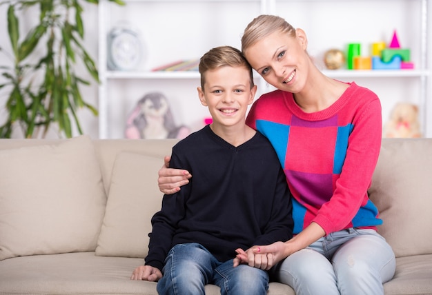 Hermosa madre y su hijo está sentado en el sofá en casa.