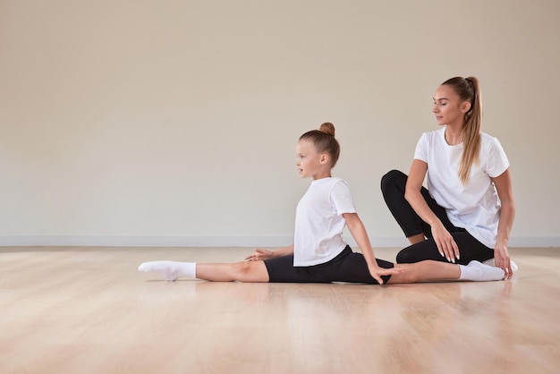 Una hermosa maestra ayuda a una niña a estirarse en una clase de gimnasia El concepto de educación deportes Pilates estiramiento estilo de vida saludable Medios mixtos