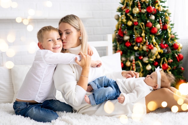 Hermosa mamá con dos hijos celebran Navidad Año Nuevo en casa con árbol de Navidad