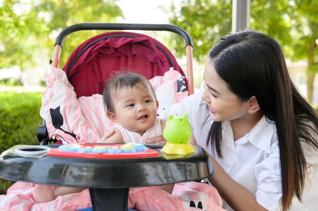 Hermosa mamá con una niña sentada en un carrito de bebé al aire libre en el día del sol