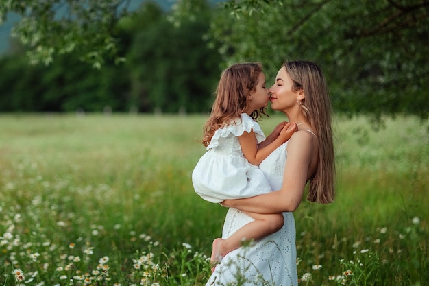 Foto hermosa mamá su pequeña hija con vestidos blancos se divierte en un paseo en verano