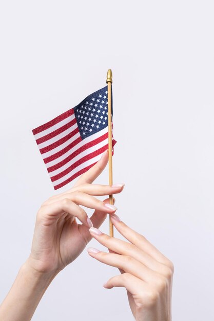 Una hermosa mano femenina sostiene una bandera estadounidense sobre un fondo blanco.