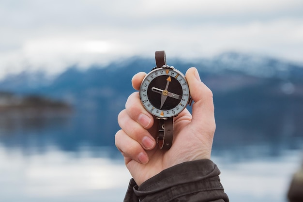 Una hermosa mano masculina sostiene una brújula magnética contra el fondo de la montaña y un lago