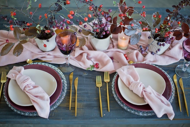 Hermosa mesa con servilletas rosas y corredor rosa tenedores y cuchillos dorados velas y hojas de otoño y bayas