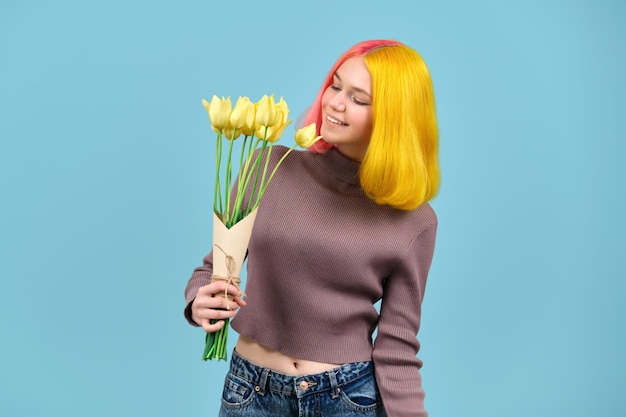 Hermosa modelo adolescente sonriente con ramo de tulipanes amarillos sobre fondo azul.