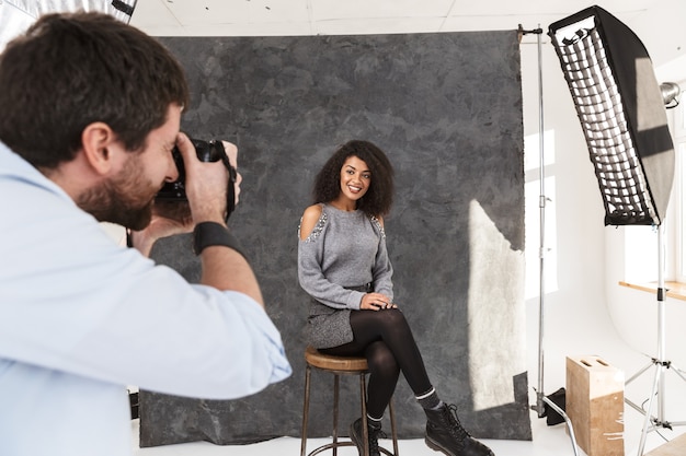 Foto una hermosa modelo africana que presenta al fotógrafo con la cámara toma una sesión en una sesión de backstage en el estudio.