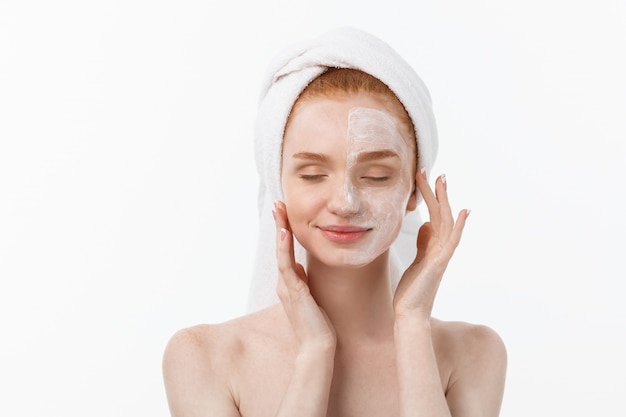 Hermosa modelo aplicando el tratamiento de crema cosmética en la cara en blanco.