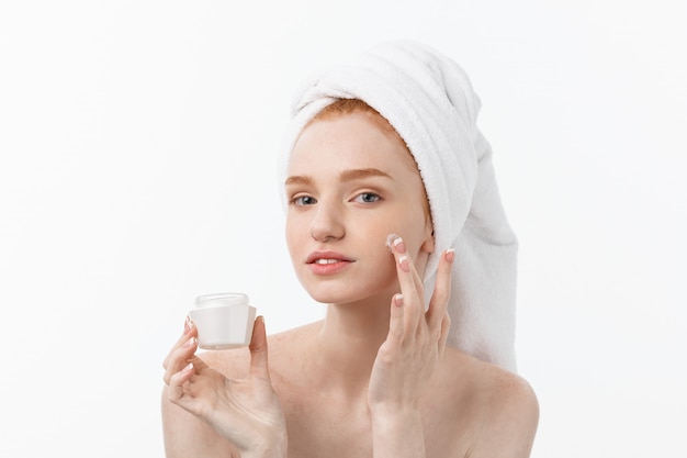 Hermosa modelo aplicando el tratamiento de crema cosmética en la cara en blanco.