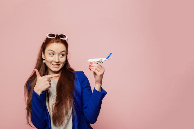 Hermosa modelo femenina sonriente divertida señala con un dedo al avión