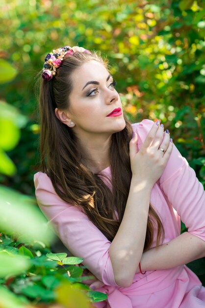 Foto hermosa modelo femenina vestida con un largo vestido rosa posa entre las muchas flores en el invernadero