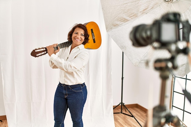 Hermosa modelo de guitarrista posando frente a la cámara profesional sosteniendo la guitarra en el estudio.