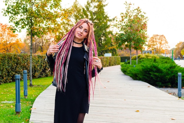 Hermosa modelo con largas rastas y coletas vestidas de negro camina por el parque