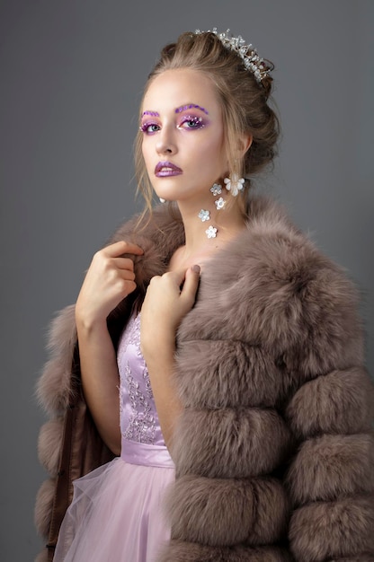 Hermosa modelo con maquillaje de moda en un abrigo de piel Chica de invierno de lujo sobre un fondo gris