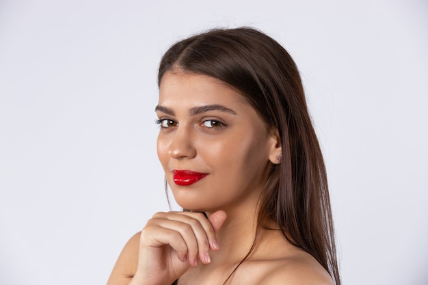 Una hermosa modelo morena con labios rojos mira a la cámara. Concepto de belleza y maquillaje. Foto en pared blanca.