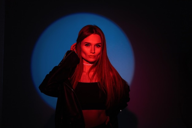 Hermosa modelo de mujer creativa con estilo en ropa de moda con luz roja sobre fondo azul oscuro en el estudio