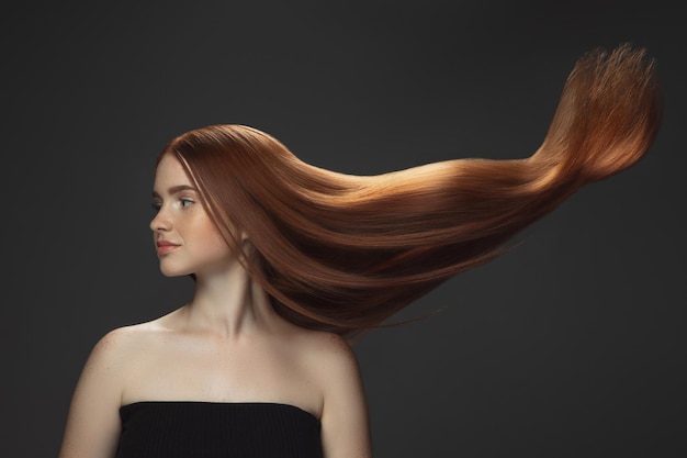 Hermosa modelo con pelo rojo largo, liso y volador aislado en estudio oscuro