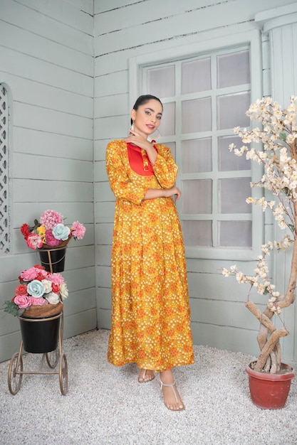 Hermosa modelo posando con confianza para una sesión de moda en interiores con flores y vestido floral