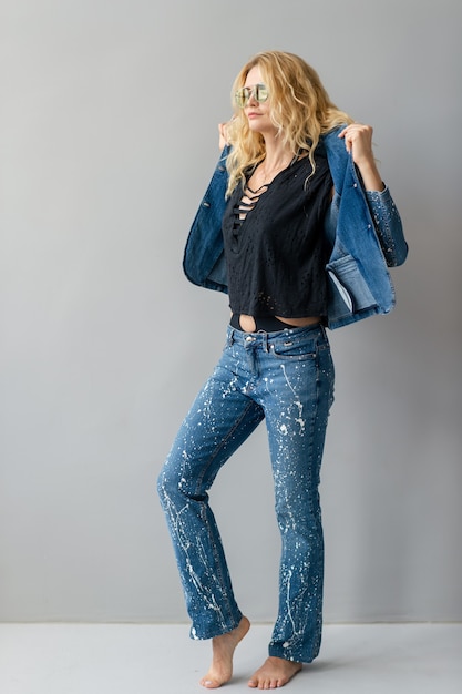 Hermosa modelo rubia con estilo en traje de jeans posando en estudio