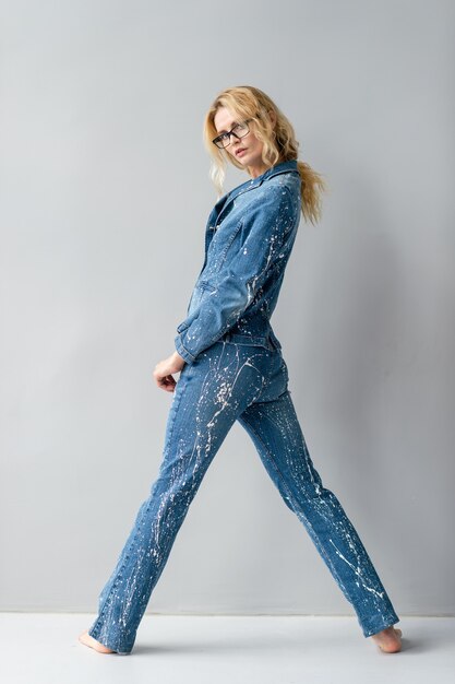 Hermosa modelo rubia con estilo en traje de jeans posando en estudio