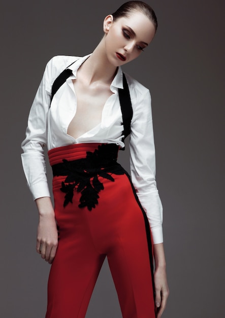 Hermosa modelo vistiendo pantalones rojos y camisa blanca sobre fondo gris