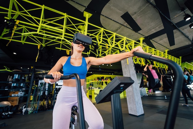 Hermosa morena en una bicicleta estática con gafas de realidad virtual