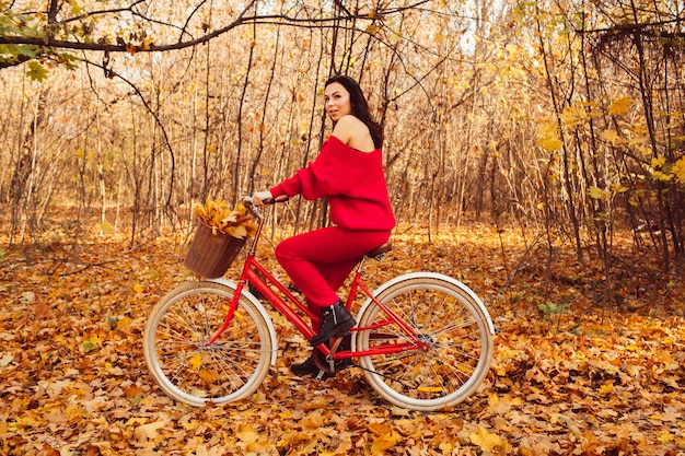 Hermosa morena en el bosque de otoño con una bicicleta