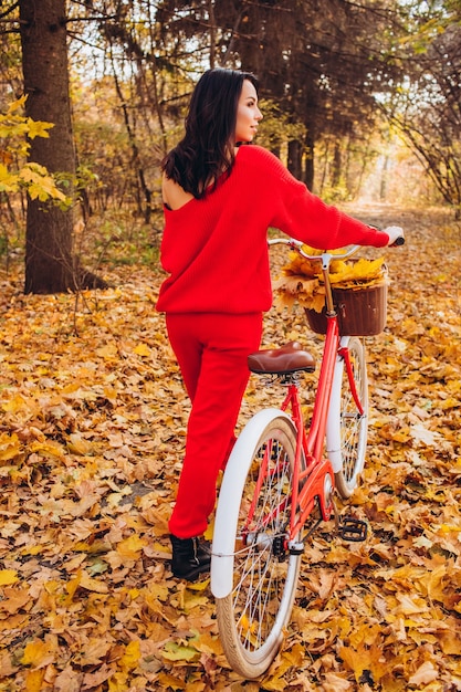 Hermosa morena en el bosque de otoño con una bicicleta