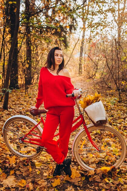 Hermosa morena en el bosque de otoño con una bicicleta