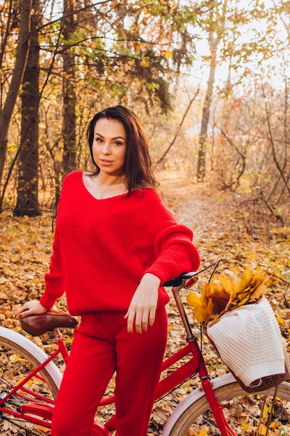 Hermosa morena en el bosque de otoño con una bicicleta