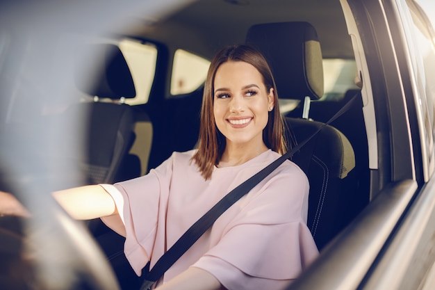 Hermosa morena caucásica con gran sonrisa toothy conducir coche. Manos en el volante.