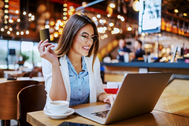 Hermosa morena caucásica sonriente de moda sentada en la cafetería