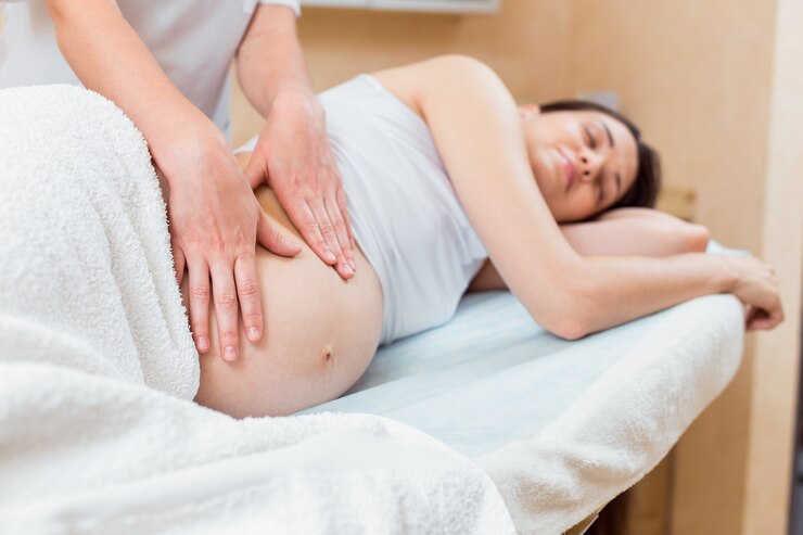 Una hermosa morena embarazada con cabello largo yace de lado en una recepción con un terapeuta de masaje en una sala de cosmetología.