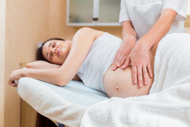 Una hermosa morena embarazada con cabello largo yace de lado en una recepción con un terapeuta de masaje en una sala de cosmetología.