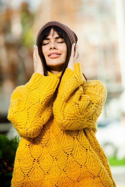 Hermosa morena europea vestida con un suéter de lana amarillo y un sombrero afuera