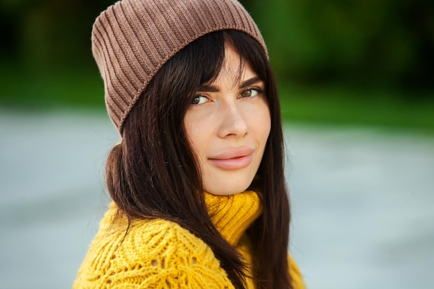 Hermosa morena europea vestida con un suéter de lana amarillo y un sombrero afuera