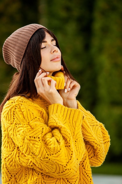 Hermosa morena europea vestida con un suéter de lana amarillo y un sombrero afuera