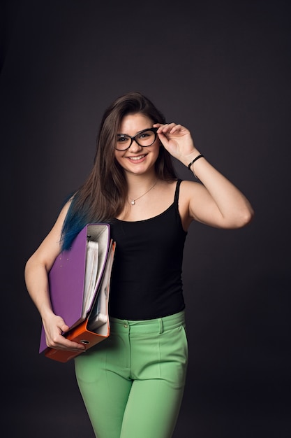 Hermosa morena joven en gafas y pantalones verdes con carpetas