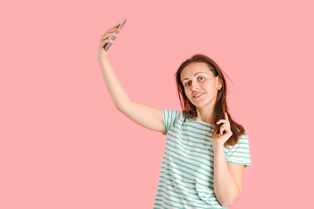 Una hermosa morena de mediana edad se toma un selfie posando sobre un fondo rosa