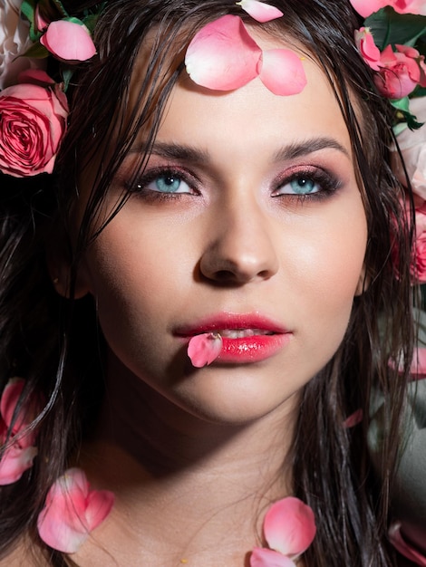 Hermosa morena de ojos azules con maquillaje rosa brillante acostado rociado con pétalos de rosa rosa closeup sp...