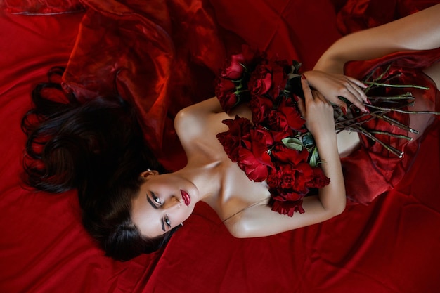 Hermosa morena sexy con un ramo de rosas rojas en el suelo, partes del cuerpo desnudo, retrato erótico de una mujer